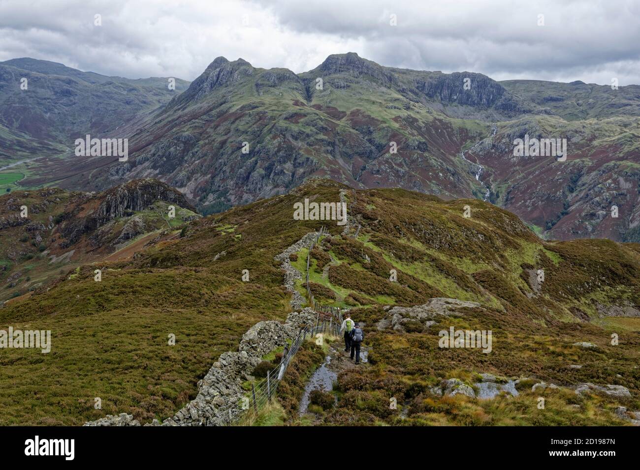 Two fell walkers descending Lingmoor Fell in the English Lake District as they follow the wall to Side Pike Stock Photo