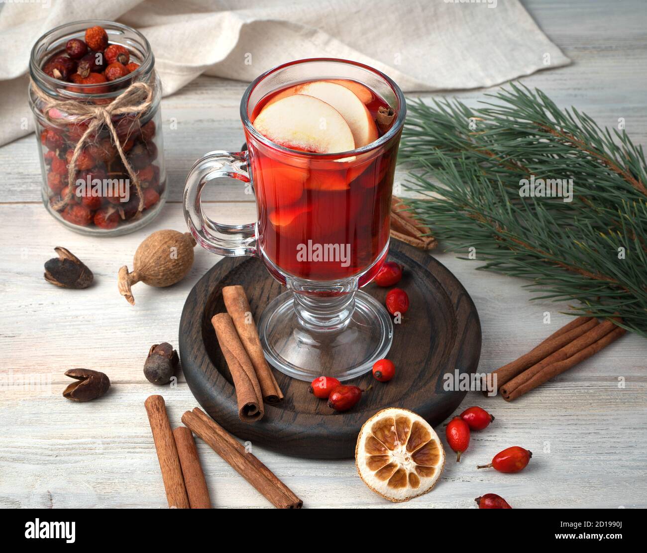 A glass of mulled wine with fruit, cinnamon and pine branches on a wooden background. Stock Photo