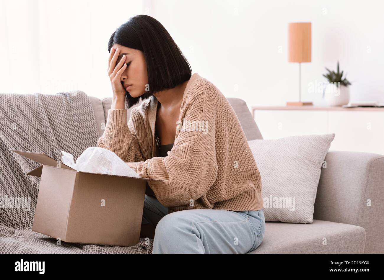 Sad young lady unpacking wrong parcel, delivery mistake Stock Photo Alamy