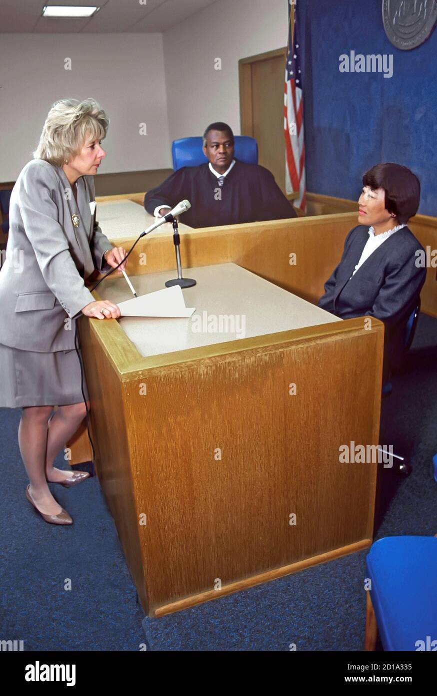 Female lawyer prosecutor questions Asian witness with black judge looking on Stock Photo