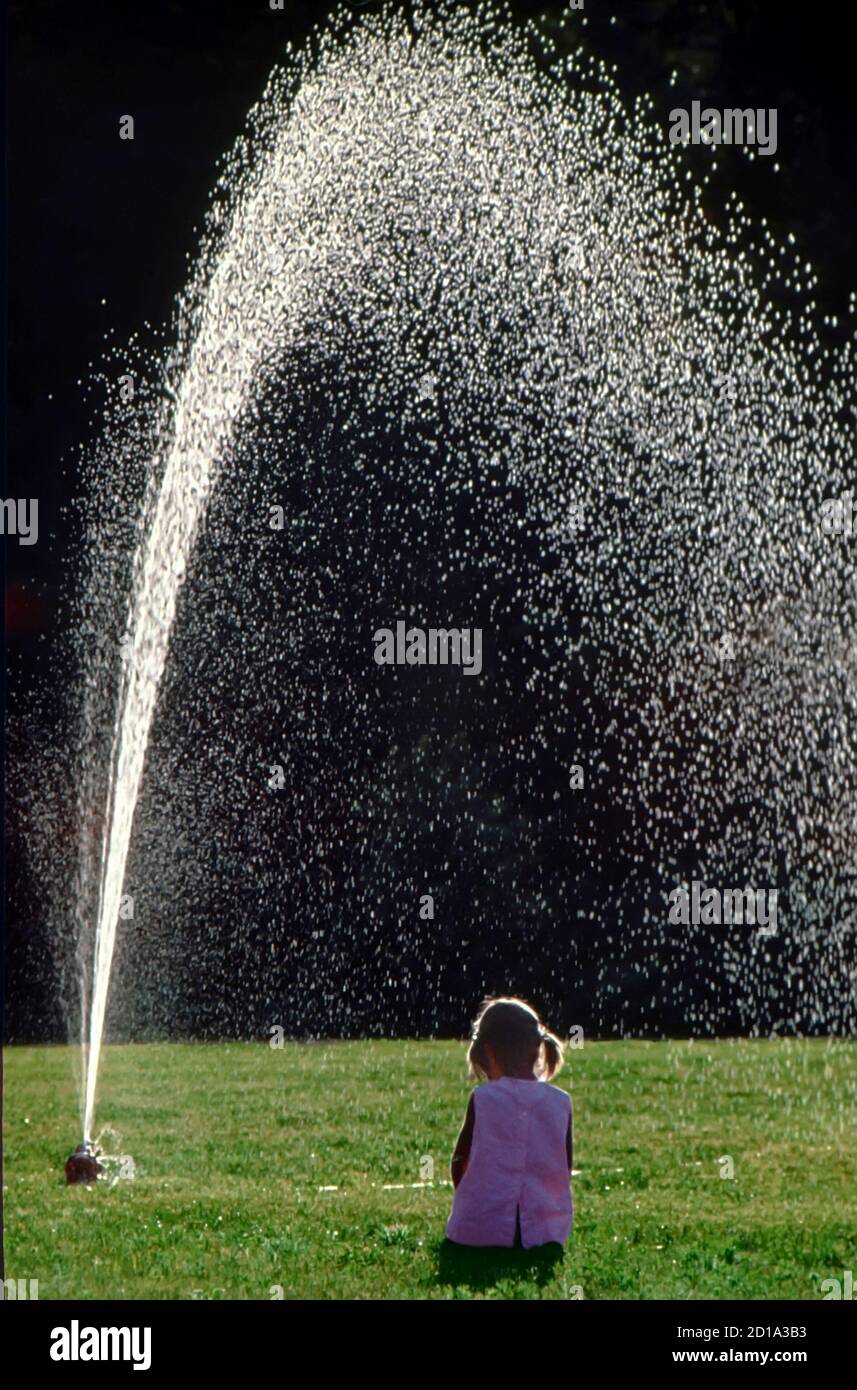 4 year old little girl  under a lawn sprinkler Stock Photo