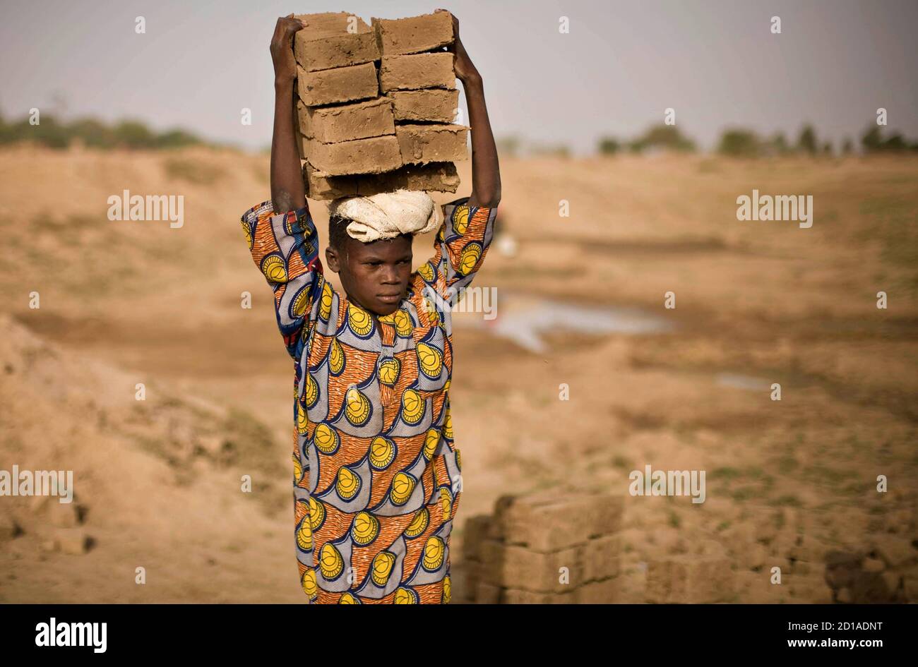 A boy carries bricks on his head at a riverside factory where mud is fired in kilns to produce building materials on the outskirts of Chad's capital N'Djamena, May 31 2008. Many children are used as cheap labour to transport bricks. REUTERS/Finbarr O'Reilly (CHAD) Stock Photo