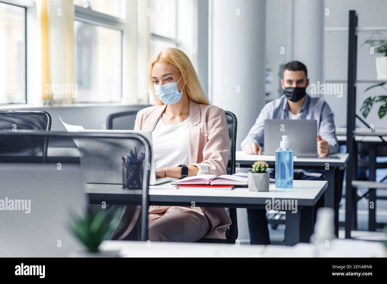 New working conditions and social distancing after covid-19 quarantine. Blonde woman in protective mask works with documents and laptop Stock Photo