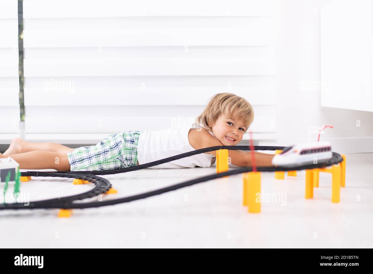 Cute kid boy laying down on the floor and playing with toy railway road ...