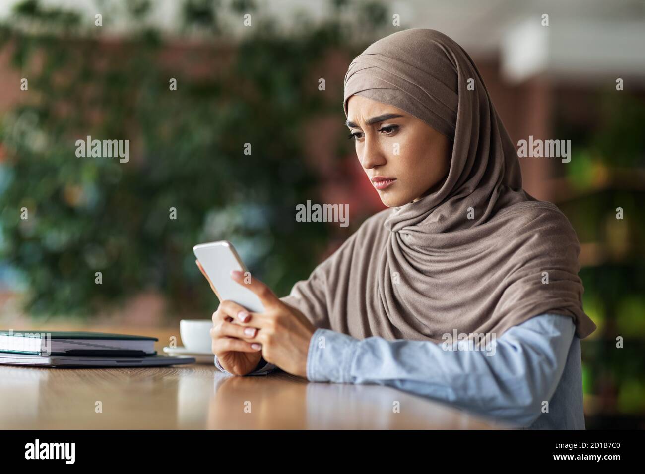 Serious woman in hijab using smartphone while resting at cafe Stock ...