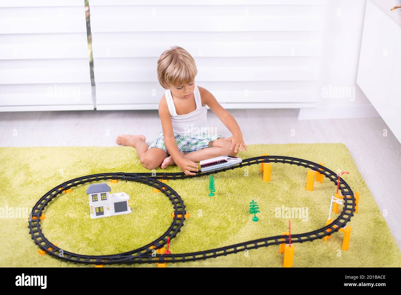 Little boy play with plastic railway. Child with toy train. Educational toys for young children. Little boy building railroad tracks on green carpet. Stock Photo