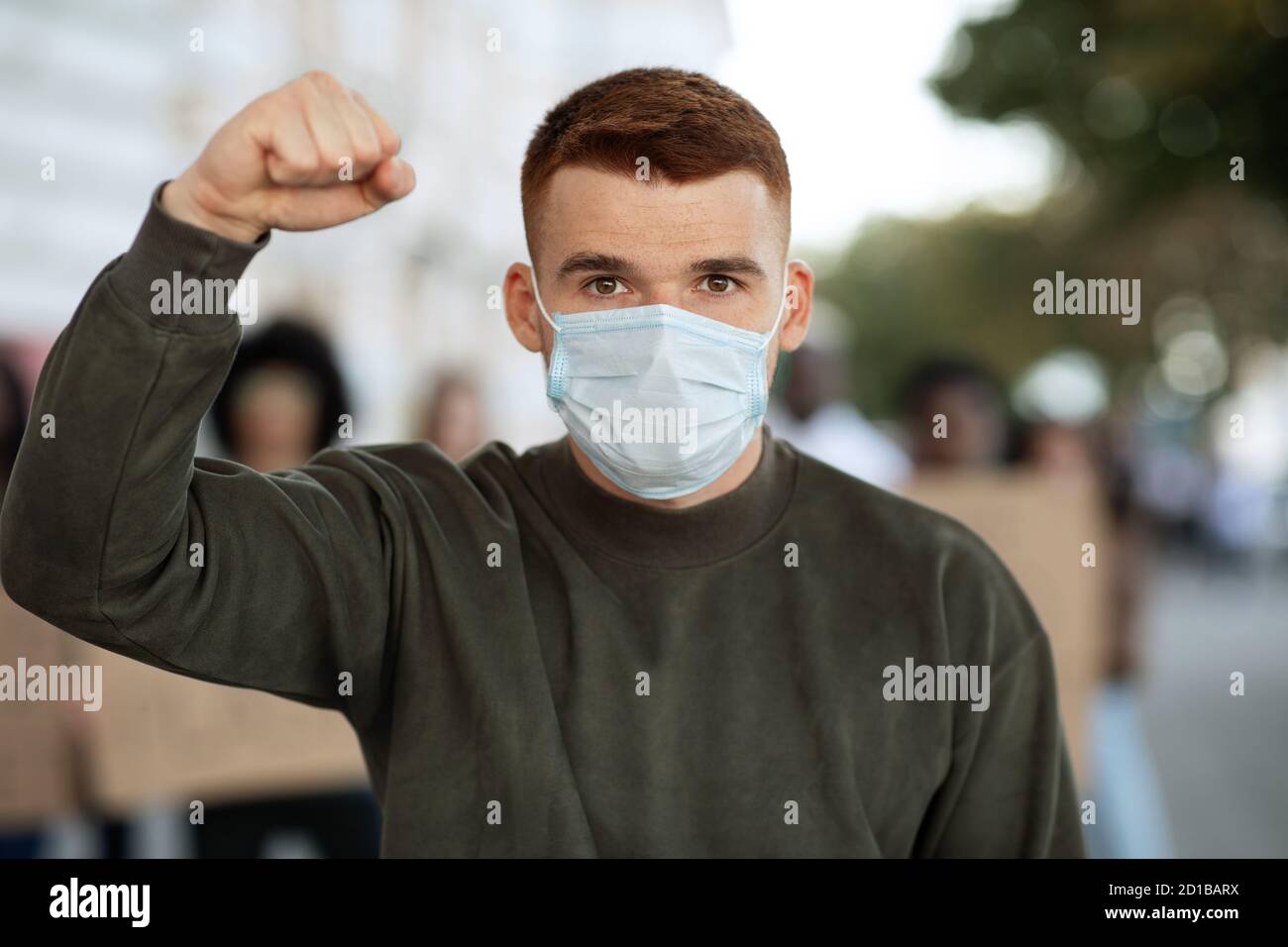 Guy in face mask gesturing over group of demonstrators Stock Photo
