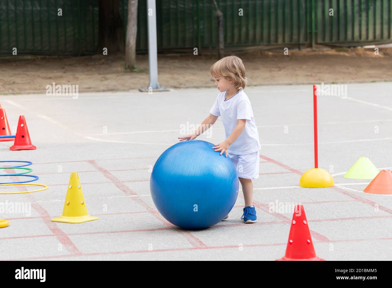 Beautiful little boy rolling the big blue ball on sports polygon Stock Photo