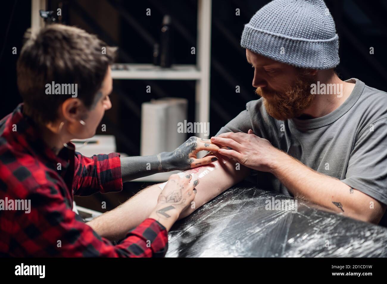 A tattoo artist bandages the young man's hand with a thin layer of