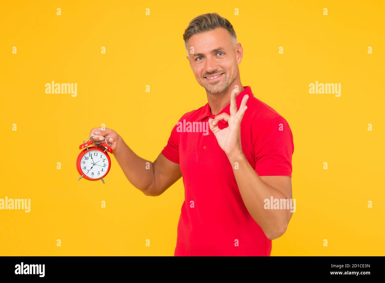 All right. Happy man hold alarm clock showing OK sign. Punctuality and accurate timekeeping. Chronometry and timekeeping. Clock gives the right time. Stock Photo