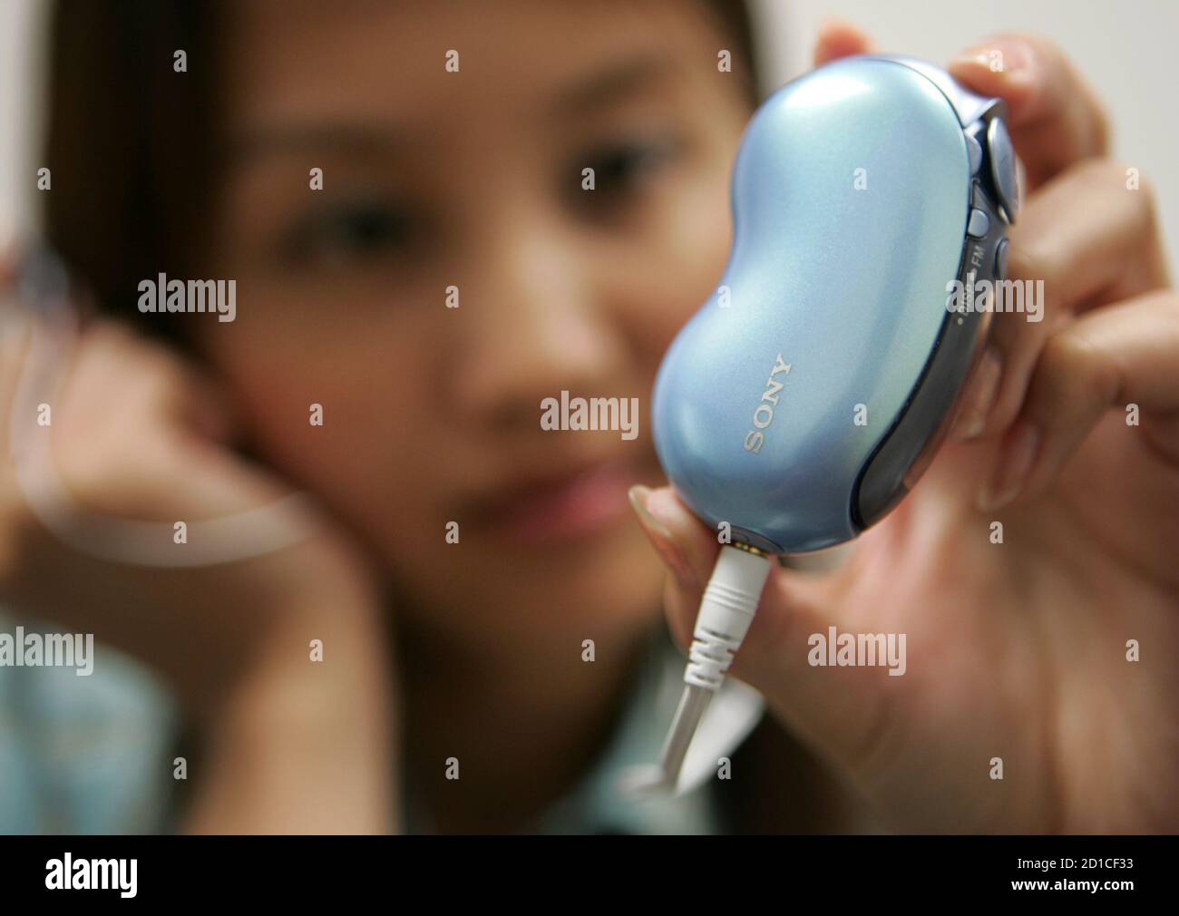 Sony Marketing Japan Inc. employee Zhang Wen puts on the earphones on a the  latest portable digital music player Walkman Bean MP3 mock-up at company  headquarters in Tokyo August 26, 2005. Shaped