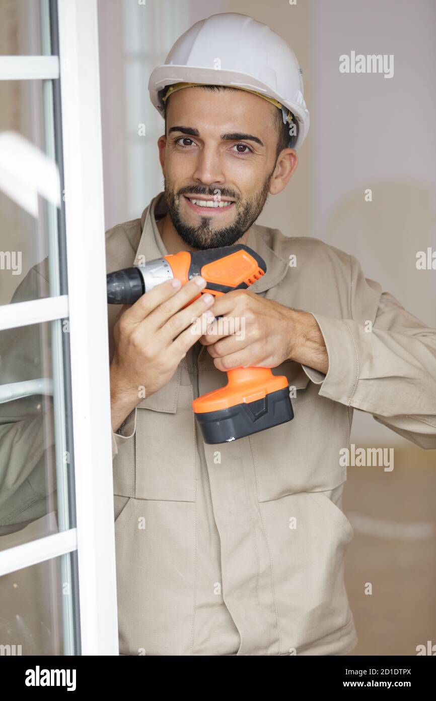 smiling man fixing a window handle using cordless screwdriver Stock Photo
