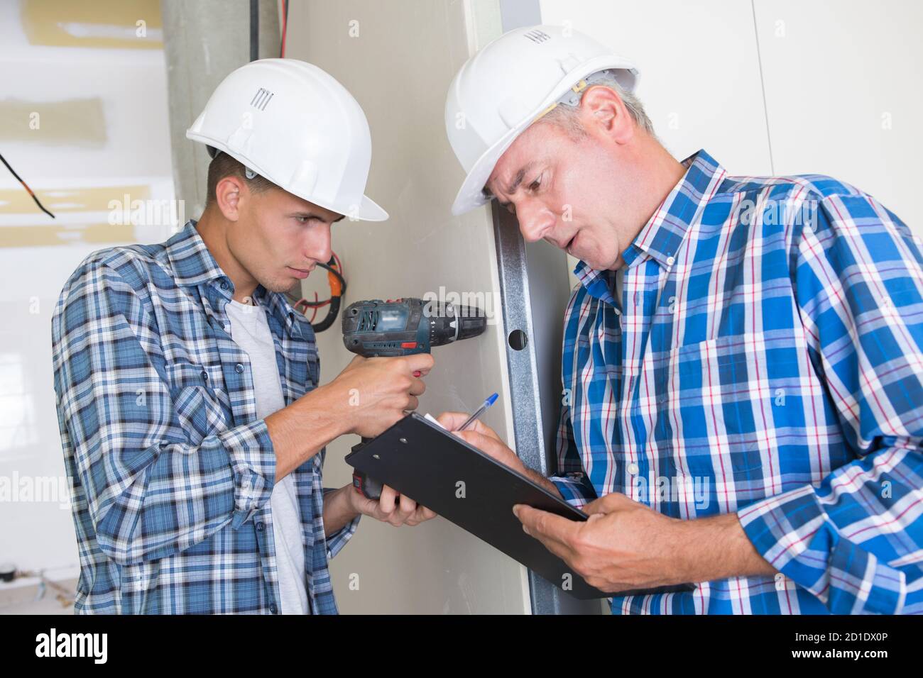young workman using drill while supervisor fills in paperwork Stock