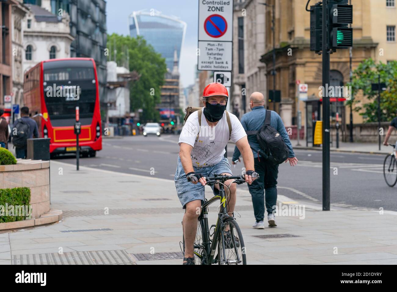 LONDON, ENGLAND - JUNE 3, 2020: Elderly male cyclist riding a bicycle in Holborn London wearing a face mask, glasses and crash helmet during the COVID Stock Photo