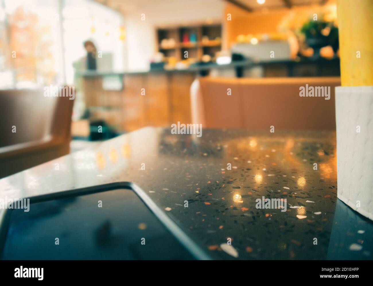 Modern blurred coffee shop Scene. Phone and coffee cup on table as foreground. Soft blurred sofa chair, bar / counter shelves and window front in the Stock Photo