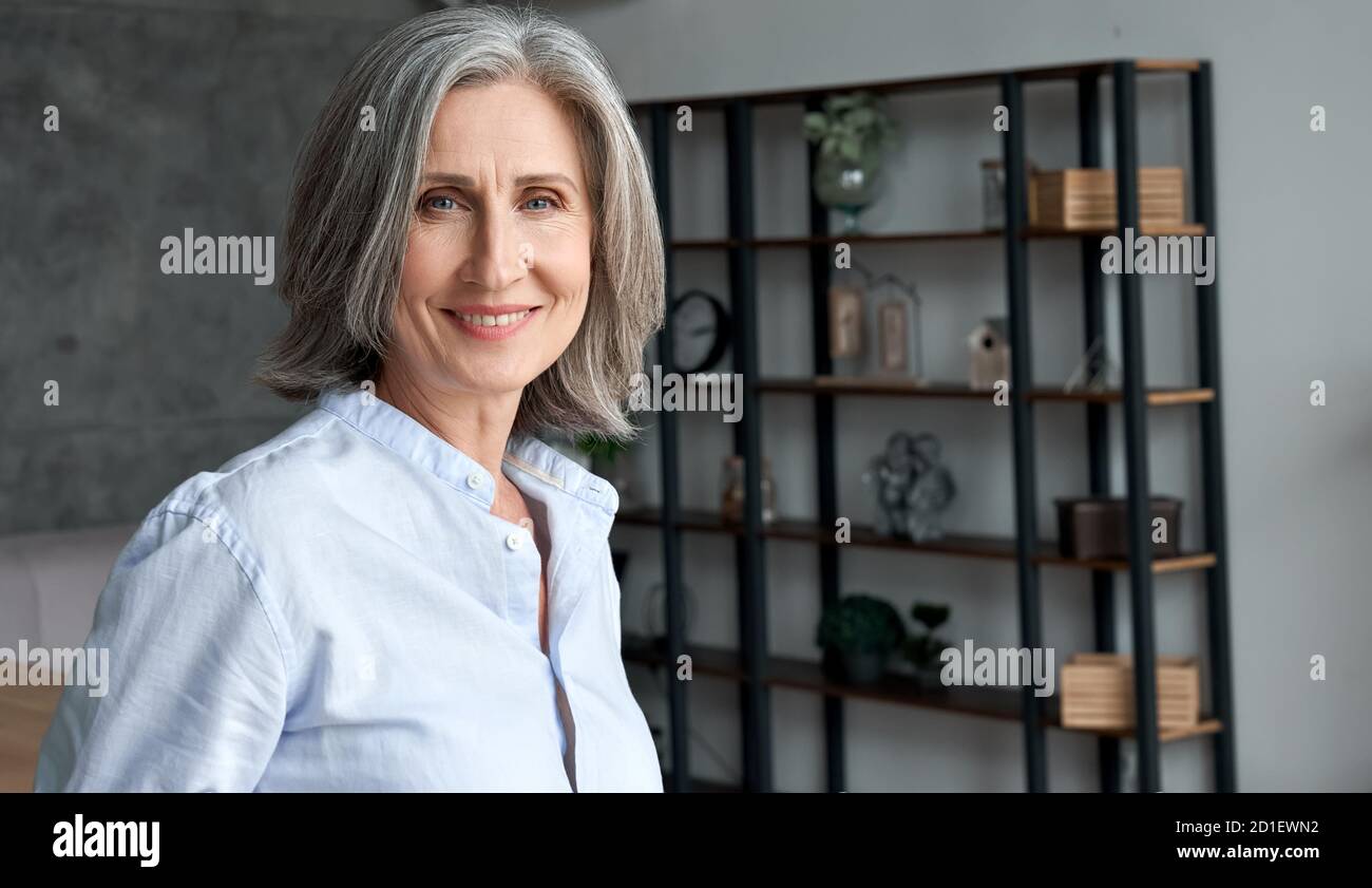 Smiling confident middle aged grey-haired woman standing in office, portrait. Stock Photo