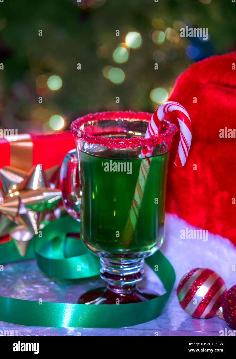 This festive holiday drink is set next to a santa hat on Christmas eve. Green punch with a red sugar rim and a candy cane, makes a perfect Christmas n Stock Photo