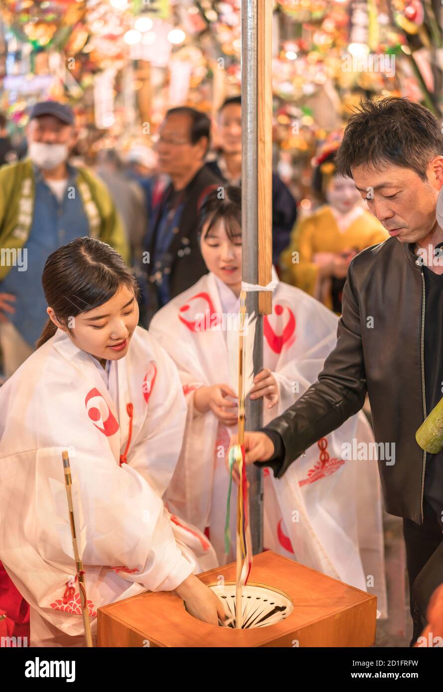 asakusa, japan - november 08 2019: Japanese Miko maiden in traditional religious shōzoku kimono doing a lottery with a devil killing arrow hamaya at S Stock Photo