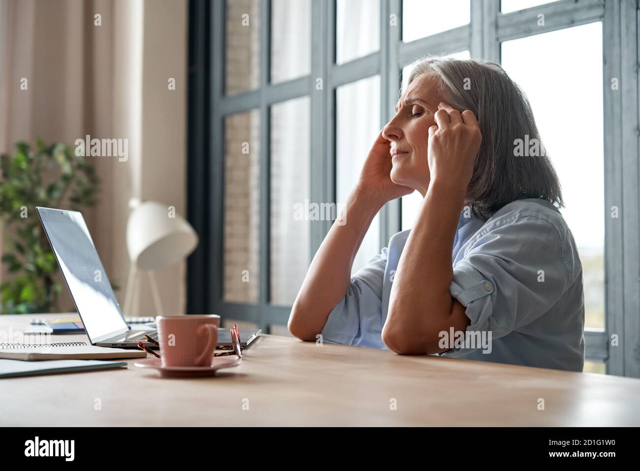 Stressed overworked old mature business woman suffering from headache at work. Stock Photo