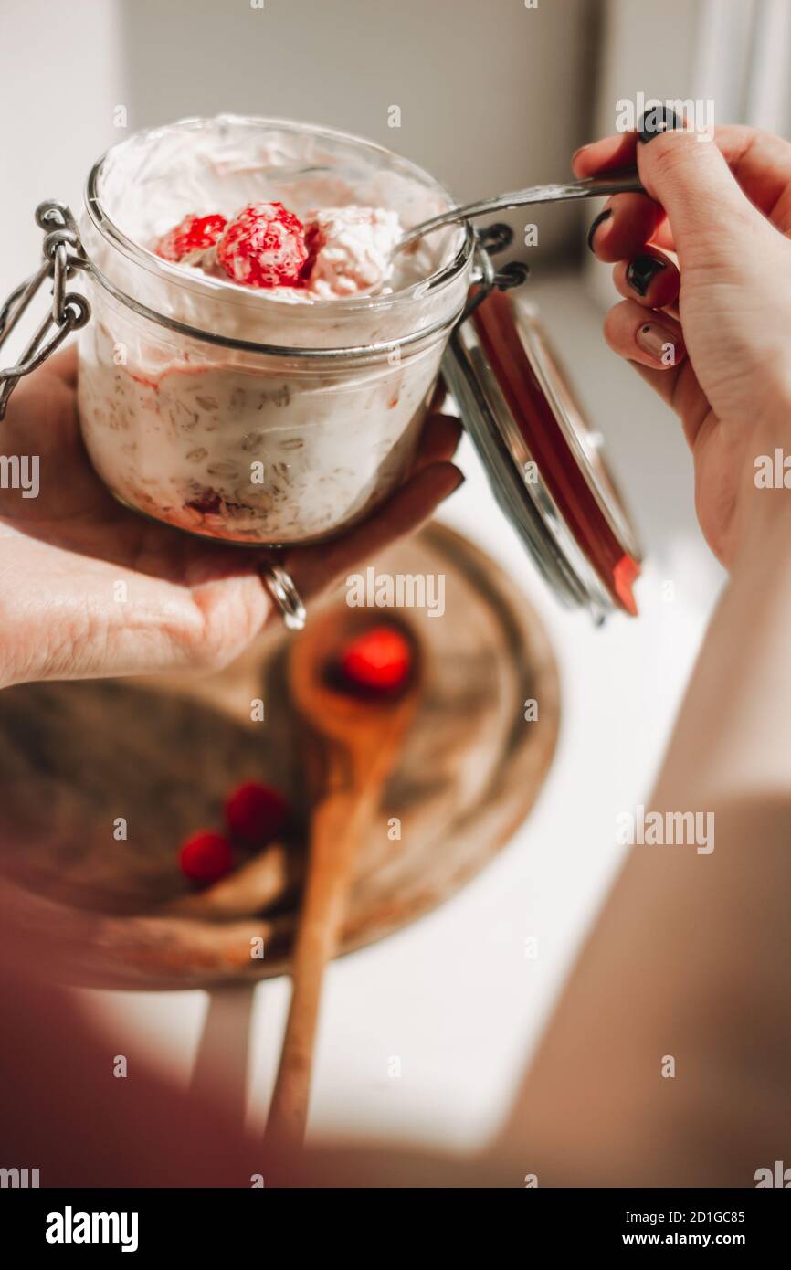 A white skin woman holding spoon of muesli in her hands with a spoonful of granola with strawberries, with nutritious oatmeal indoors on Kitchen Stock Photo