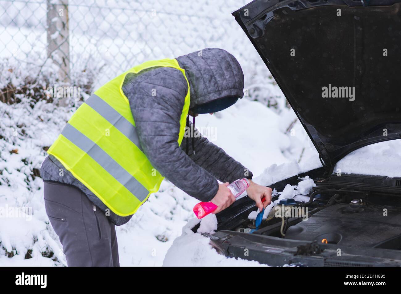 Man dressed in neon green vest pouring antifreeze coolant to car engine