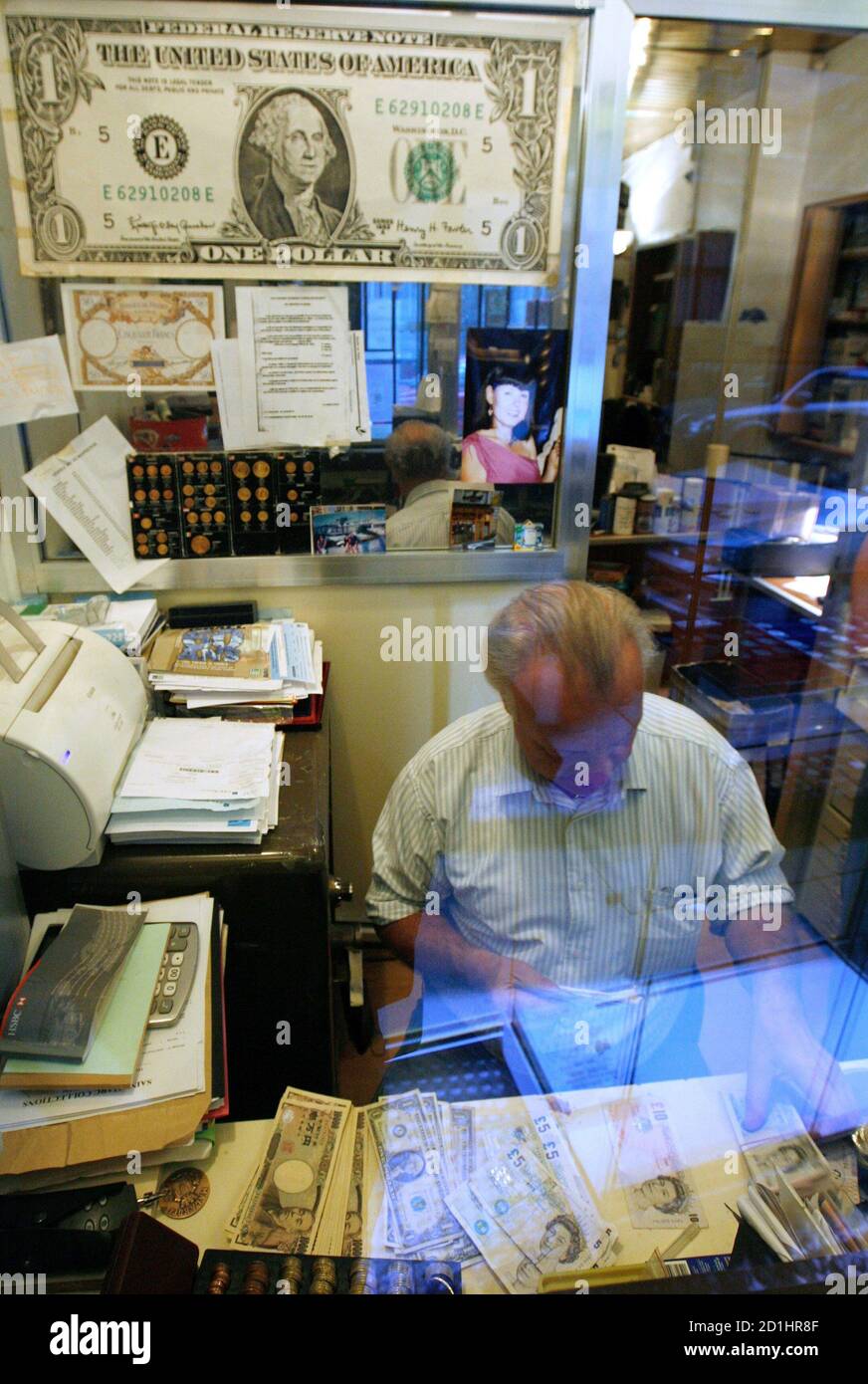 An enlarged copy of a U.S. dollar hangs on the wall above Serge Siauvaud,  who counts bills, at a currency exchange bureau in Paris September 20,  2007. The euro hit a record
