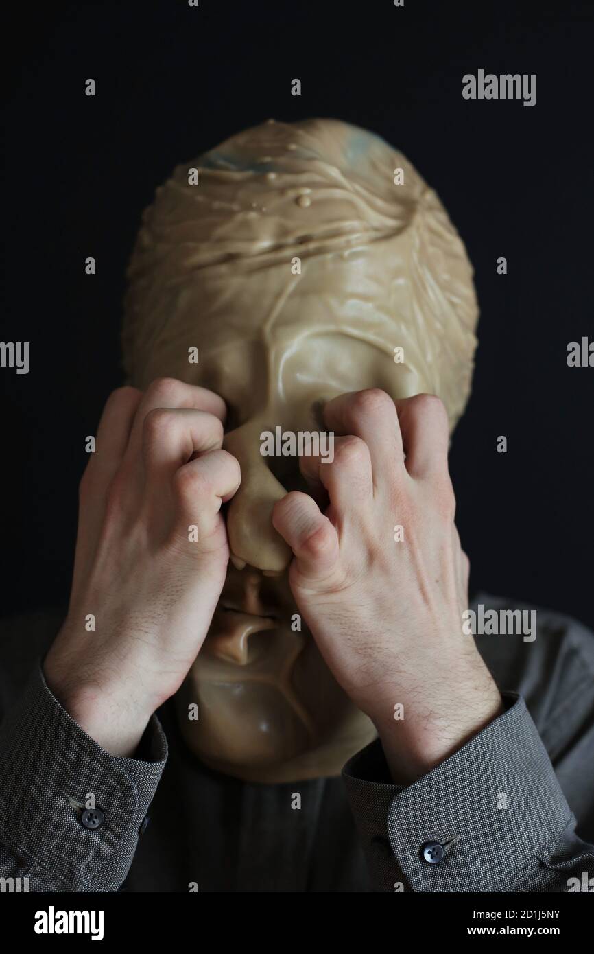 A person wearing a rubber halloween mask and clawing at their own eyes. Stock Photo