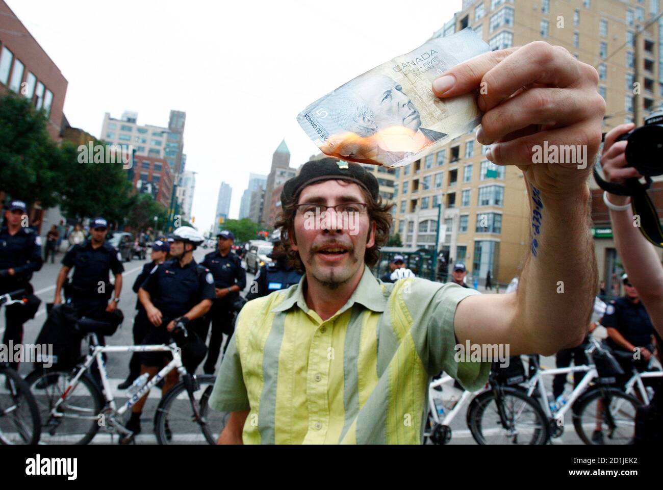 A man burns a Canadian five-dollar note during a protest at the G20 summit in Toronto June 27, 2010. Police in Toronto fired tear gas on protesters for a second straight day on Monday as new violence surrounding the G20 summit erupted and the arrest tally climbed toward 600. REUTERS/Christinne Muschi (CANADA - Tags: POLITICS CIVIL UNREST IMAGES OF THE DAY BUSINESS) Stock Photo