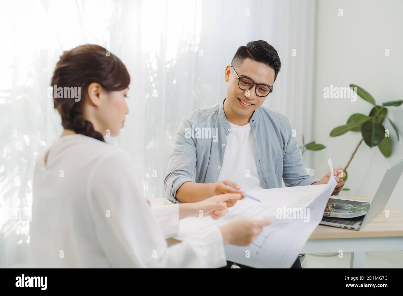 Male and female architect discussing a set of blueprints spread out on a table at office. Stock Photo