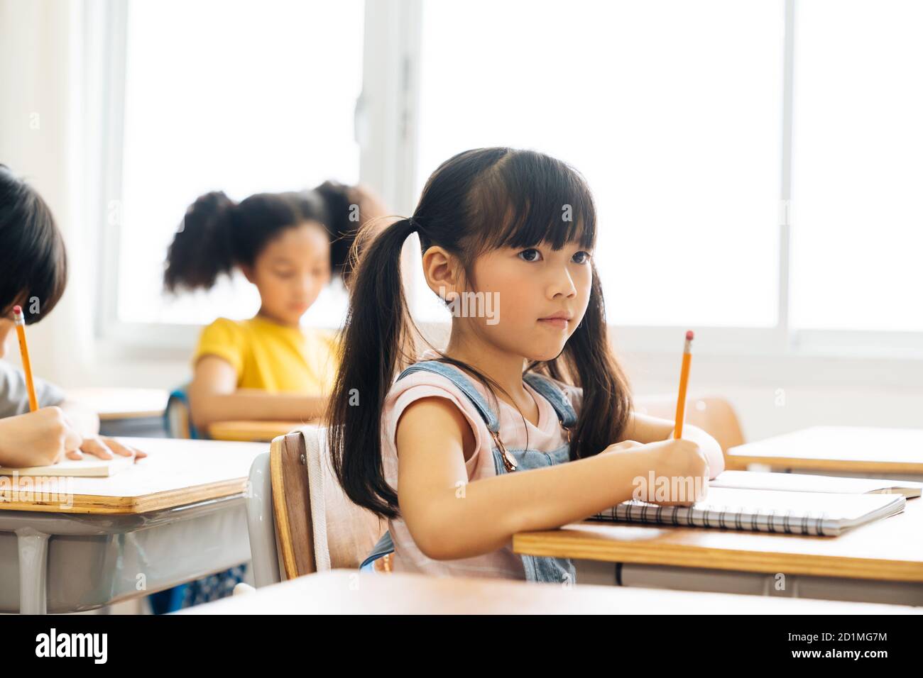 School girl sitting in school writing in book with pencil, studying, education, learning. Asian children in the class. Student diversity. Stock Photo