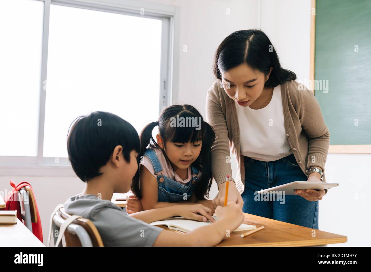 Asian school teacher using digital device with children in classroom at