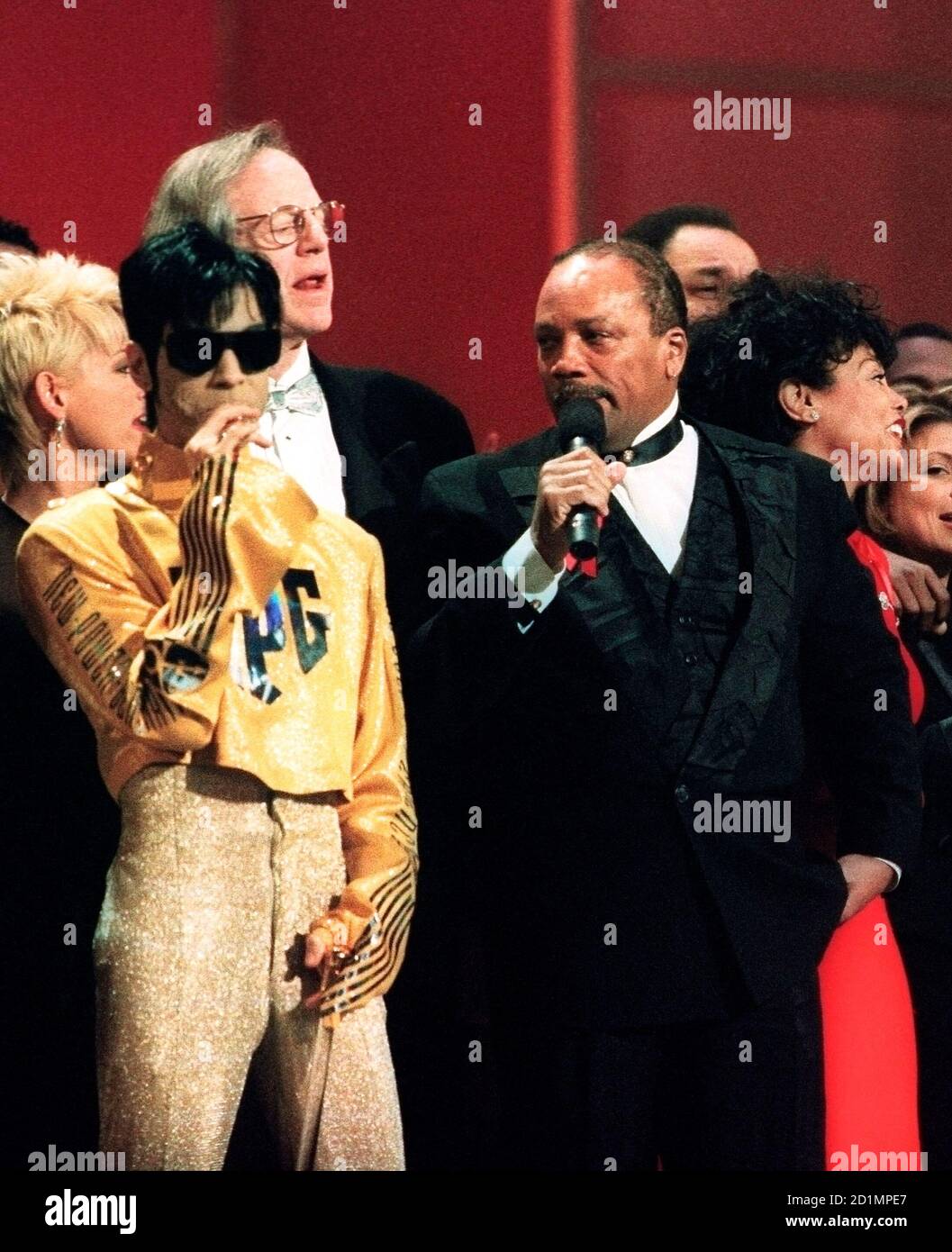 The artist formerly known as Prince (L) sucks on a lolipop as Quincy Jones and others sing 'We Are the World' January 30, 1995 at the American Music Awards.  It was the 10th anniversary of the recording of the song, which raised money for African famine relief.  Prince, who has not revealed his new name, was presented the Award of Merit.  REUTERS/Lee Celano (UNITED STATES)  BEST QUALITY AVAILABLE Stock Photo