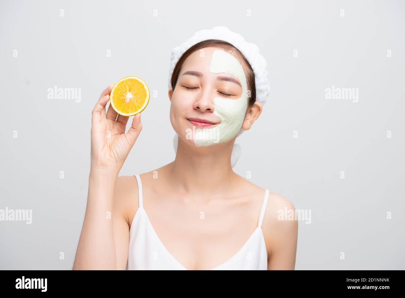 Happy young Asian woman with facial clay mask holding orange fruit
