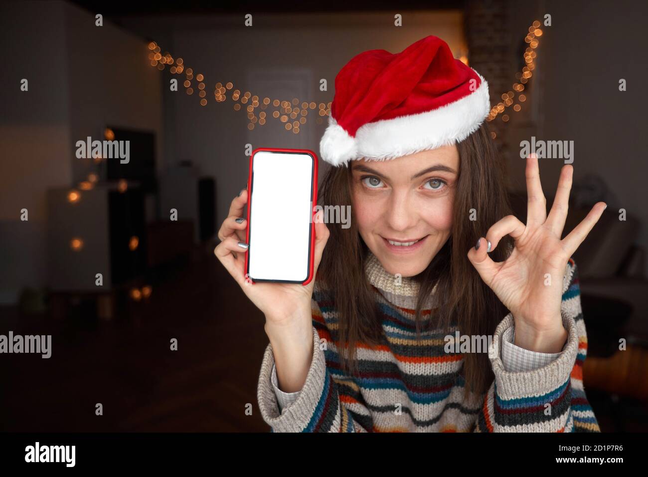 Cheerful woman showing smartphone and OK gesture on Christmas day Stock Photo