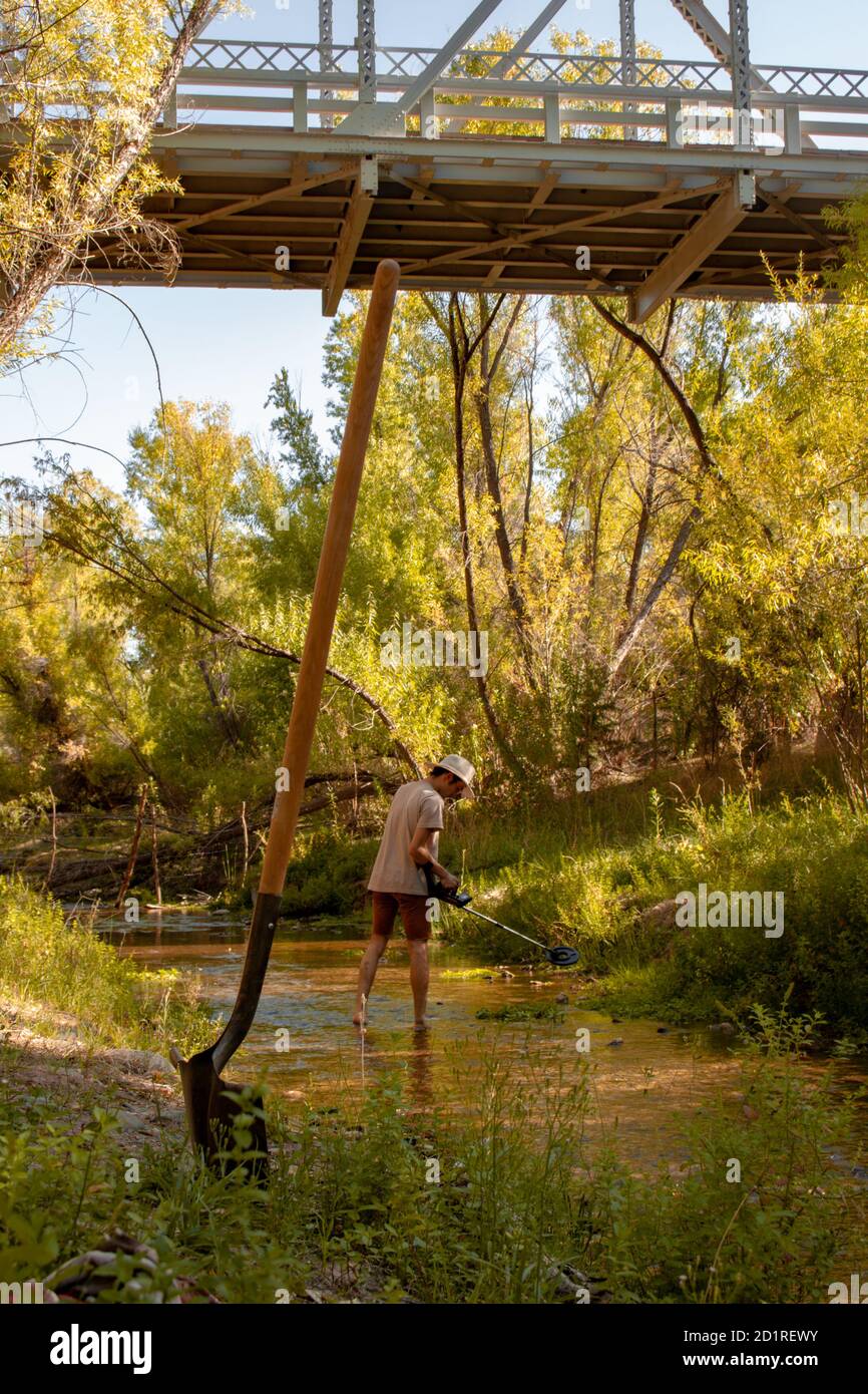 Prospector man uses a metal detector and shovel to look for lost gold treasure from the Walnut Grove Dam under the Hassayampa River Bridge in Arizona Stock Photo