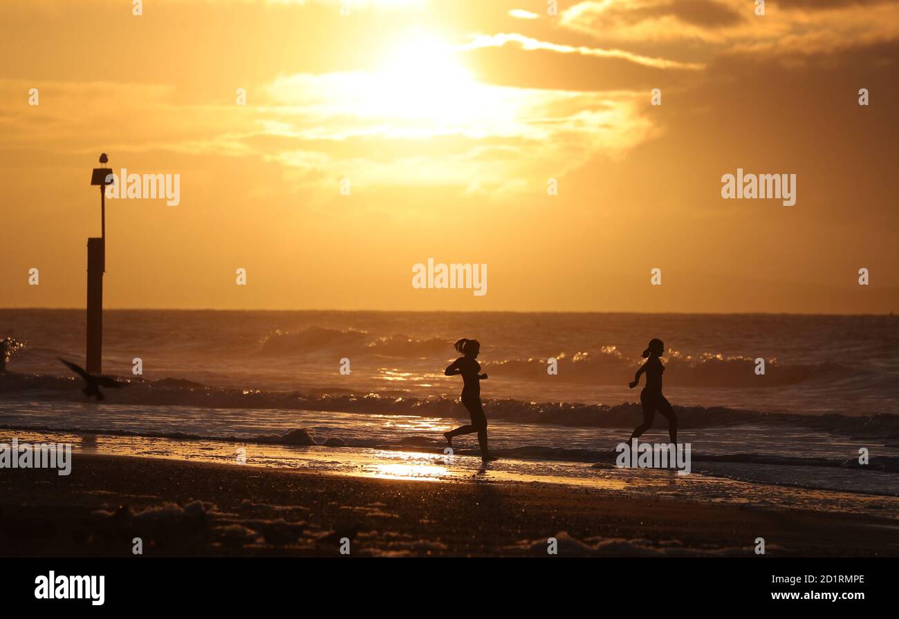 Two swimmers run into the sea as the sun rises over Boscombe beach in Dorset. Stock Photo