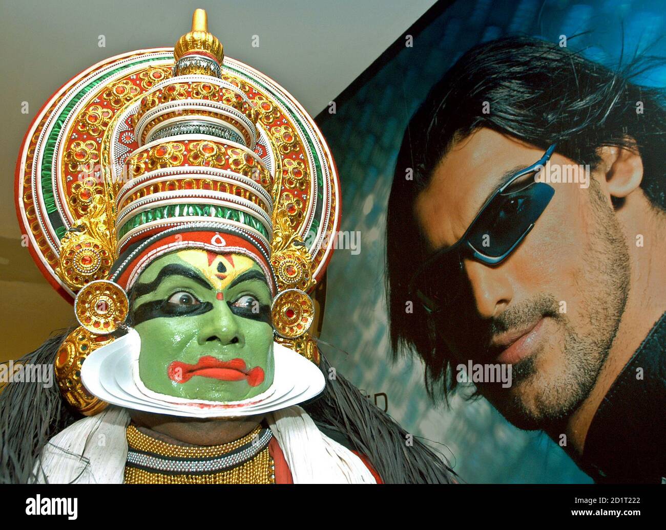 An Indian artiste sits next to a poster of actor John Abraham after  performing a traditional dance, 