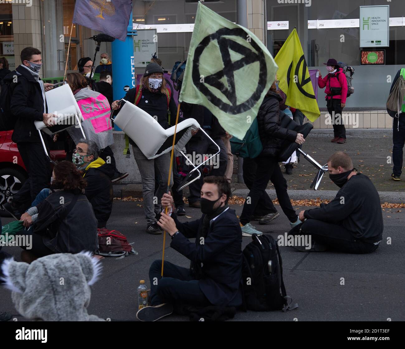 Berlin, Germany. 06th Oct, 2020. Participants of a protest action of the environmental protection alliance Extinction Rebellion (XR) carry chairs onto the street in front of the Haus der Wirtschaft in the Berlin district Charlottenburg, an activist holds a flag with the XR logo. Credit: Paul Zinken/dpa/Alamy Live News Stock Photo