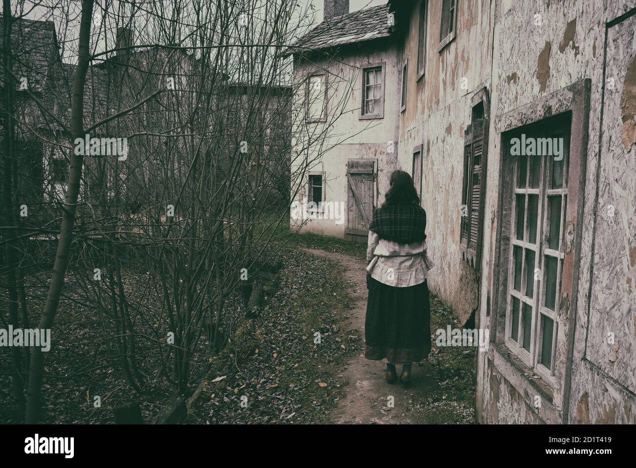 A woman with a shawl on her shoulders walks along the path of an old sad city in medieval Europe Stock Photo