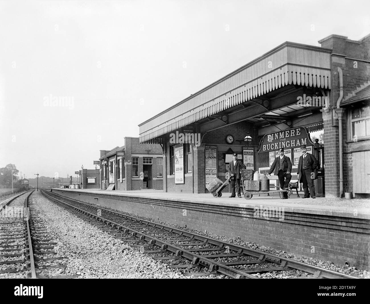 FINMERE STATION, Oxfordshire. The Great Central Railway Company built this station on the line from Sheffield through Nottingham and Leicester to London in 1898-9. A new Great Central Railway terminus was built at Marylebone. Behind these porters are posters advertising tickets for trips to London. These journeys would be unthinkable for most people before the coming of the railways. Photographed by Alfred Newton and Son in 1904. Stock Photo