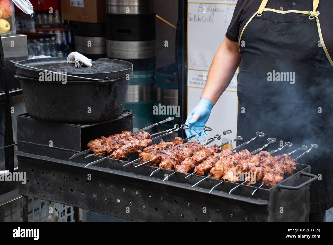 Close up of meat skewer, grilled in a barbecue, shashlik or shashlyk of pork for a picnic, man preparing and roasting in a street market, ready to eat Stock Photo