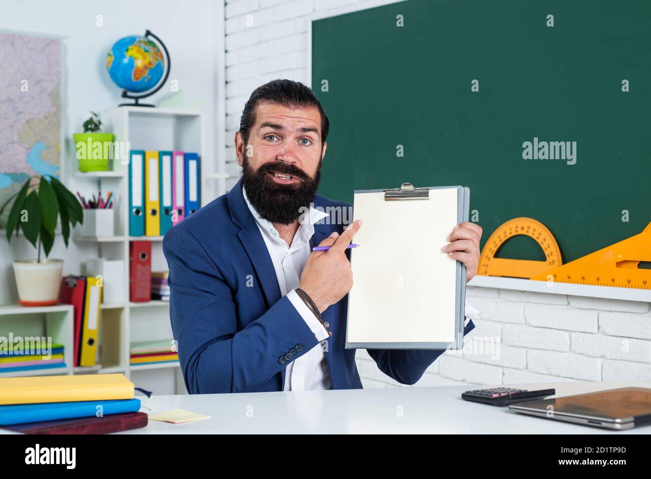 brutal bearded man work in classroom with documents and pointing on copy space, school education. Stock Photo