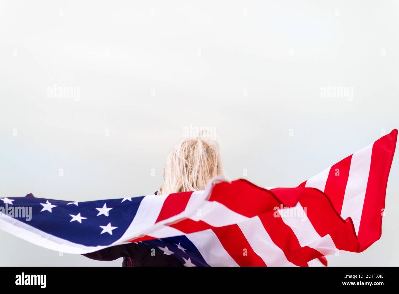 Caucasian blonde woman holding american flag leaning against back and looking at sea. Usa flag for independence day Stock Photo
