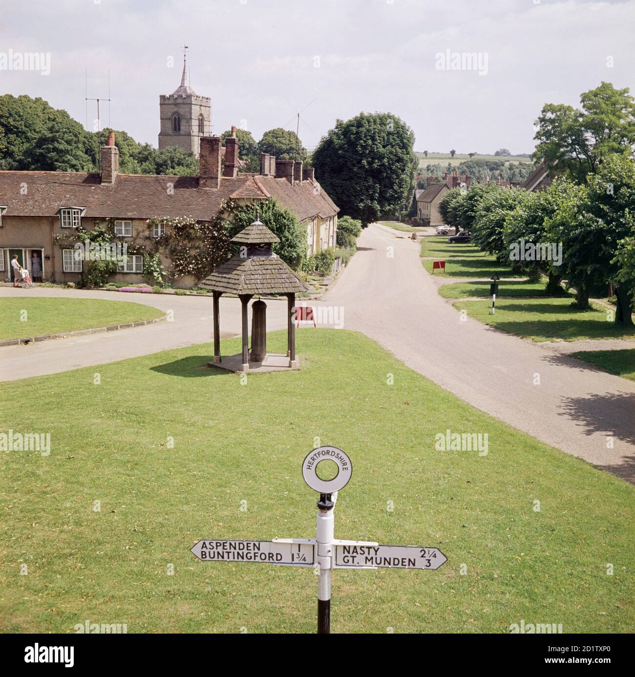WESTMILL, Hertfordshire. View of the village green and roofed village pump in Westmill. In the background, houses on Pilgrims Close with the tower of St Mary's Church beyond. In the foreground is the top half of a Hertfordshire finger post including the placename Nasty.  Photographed by John Gay in 1973. Stock Photo