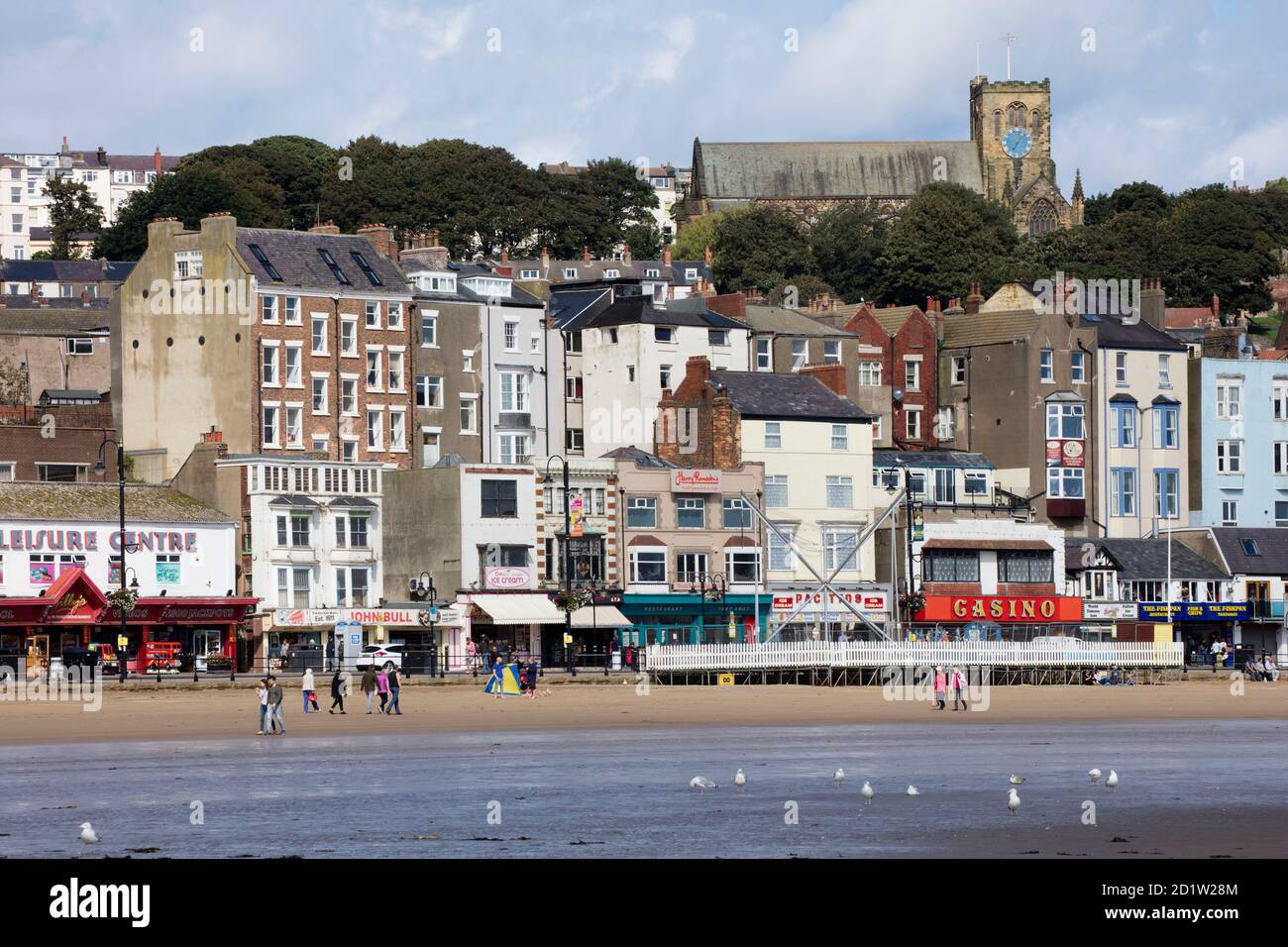 General view looking north-west from the beach towards shops, cafes and amusement arcades at the north end of the street, with St Mary's Church in the background, Scarborough, North Yorkshire, UK. Stock Photo