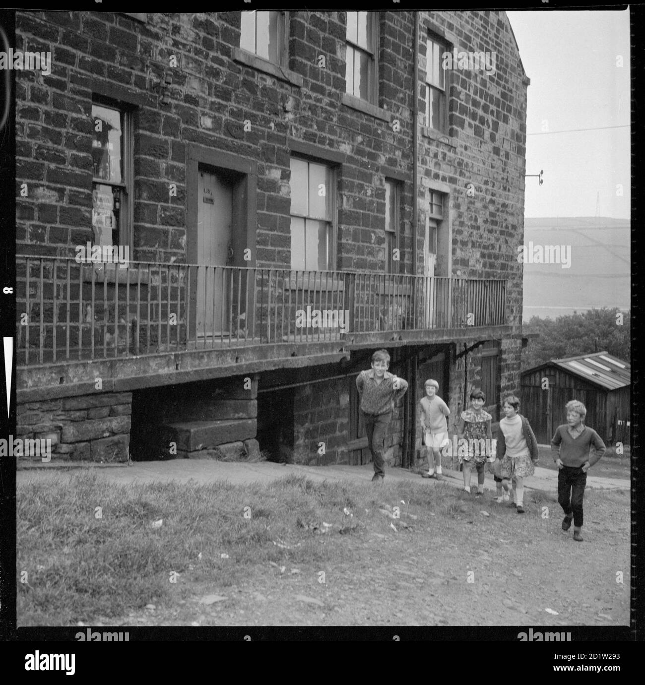 A group of children walking past the side elevations of back-to-back houses at 465-467 Market Street, Whitworth, Lancashire, UK. Stock Photo