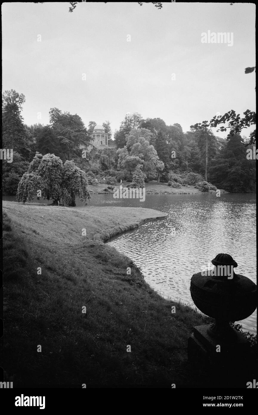 Garden lake in the grounds of Stourhead House, with the Temple of Apollo in the distance and a stone urn in the foreground, seen from a bank on the east of the lake and north of the temple, Wiltshire, UK. Stock Photo