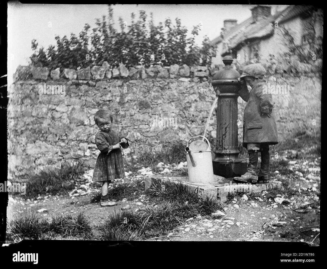 Two children collecting water at a water pump in Cheddar, Sedgemoor, Somerset, UK. Stock Photo