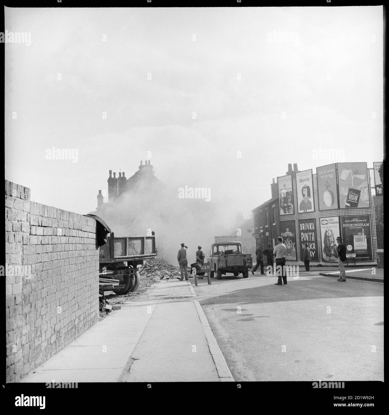 People standing, watching the demolition of houses on the east side of Lichfield Street with advertising hoardings on the corner of Boothroyd Street visible to the right. Stock Photo