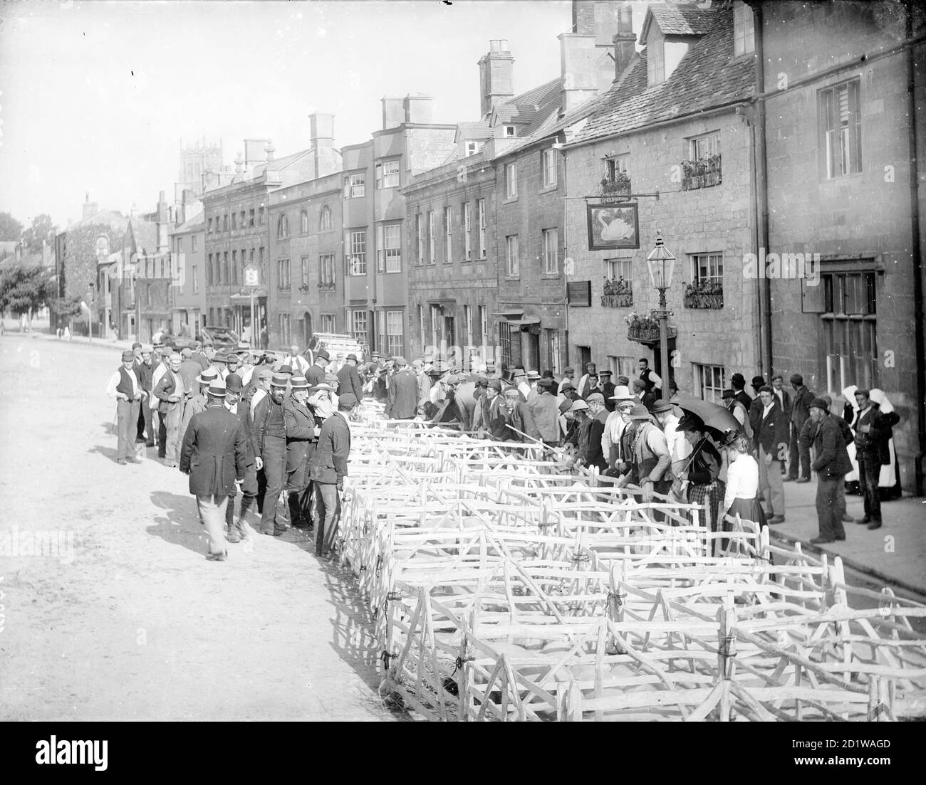 High Street, Chipping Campden, Cotswold, Gloucestershire. Looking down the street during the Pig Market outside the Swan Inn with a crowd gathered around the pig pens. Stock Photo